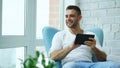 Attractive smiling man using digital tablet sitting in chair at balcony in loft modern apartment Royalty Free Stock Photo