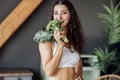 An attractive smiling vegan girl in a white top bites fresh broccoli. A curly-haired young fit woman laughs and eats cabbage at Royalty Free Stock Photo