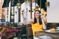 Attractive smiling woman in outdoors street coffee shop cafe sitting at table, listen music in headphones, doing selfie Royalty Free Stock Photo