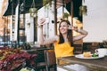 Attractive smiling woman in outdoors street coffee shop cafe sitting at table, listen music in headphones, doing selfie Royalty Free Stock Photo