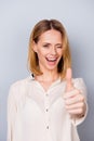 Attractive smiling woman in shirt giving a wink and showing thumb up on gray background Royalty Free Stock Photo