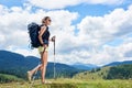 Woman hiker hiking on grassy hill, wearing backpack, using trekking sticks in the mountains Royalty Free Stock Photo