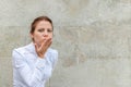 Smiling woman blowing air kiss sign gesture on urban wall background with copy space