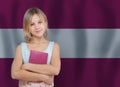 Attractive smiling yound girl with book against flag of Latvia background. Learn Latvian language concept