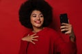 Attractive smiling young afro woman taking selfie on smartphone while standing isolated Royalty Free Stock Photo