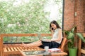 Attractive smiling young asian business woman relaxing on couch at home, working on laptop computer, talking on mobile phone Royalty Free Stock Photo