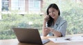 Attractive smiling young asian business woman relaxing at office, working on laptop computer, talking on mobile phone Royalty Free Stock Photo