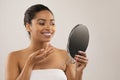 Attractive young black woman applying face cream, looking at mirror Royalty Free Stock Photo