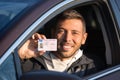 Attractive smiling young man proudly shows his driving license out of car window Royalty Free Stock Photo