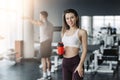 Attractive sport girl smiling and drinking water while standing at the gym with the boy training on background Royalty Free Stock Photo