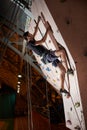 Attractive sportsman putting efforts to boulder artificial climbing wall in bouldering gym indoors.