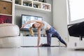 Attractive sporty woman working out at home, doing pilates exercise in front of television in her living room. Social Royalty Free Stock Photo