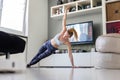 Attractive sporty woman working out at home, doing pilates exercise in front of television in her living room. Social Royalty Free Stock Photo