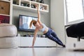 Attractive sporty woman working out at home, doing pilates exercise in front of television in her living room. Social