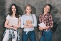 Attractive students with copybooks and laptop standing at wall Royalty Free Stock Photo