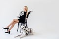 attractive stylish blonde woman in black dress sitting on chair dalmatian dog lying