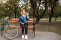 Attractive, stylish girl sitting on a bench in a park near a bicycle with a bottle of water in her hands Royalty Free Stock Photo