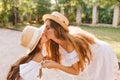 Attractive stylish woman bent over to the daughter to kiss her. Cute outdoor portrait of sweet long-haired girl in