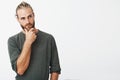 Attractive swedish guy with stylish hair and beard in grey shirt holding his chin and thoughtfully looking aside Royalty Free Stock Photo