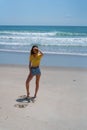 Attractive tall girl standing on beach casually with hand up shielding eyes from sun