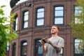 Attractive Tattooed Man Launching Drone Quadcopter and Looking At It. Stylish Red Bricked Building IS on Background