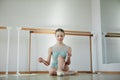 Attractive. Tender young girl, ballerina sitting on floor and putting on pointe shoes. Training in ballet school