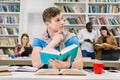 Attractive thinking handsome male student sitting at the table with many books and preparing for test or exam Royalty Free Stock Photo