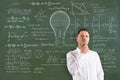 Attractive thoughtful young european businessman with abstract lamp sketch with mathematical formulas on chalkboard/blackboard Royalty Free Stock Photo