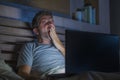 Attractive tired and stressed workaholic man working late night exhausted on bed busy with laptop computer yawning feeling sleepy Royalty Free Stock Photo