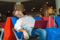 Attractive and tired traveler man with luggage taking a nap sleeping while working with laptop computer waiting for flight at Royalty Free Stock Photo