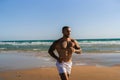 Attractive topless man with tattoos running on a beach next to a sea