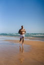 An attractive topless man with tattoos running on a beach next to a sea