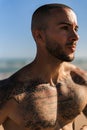 An attractive topless man with tattoos running on a beach next to a sea