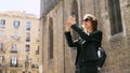 Attractive tourist woman making a selfie uses a smartfone while walking at the street.