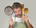 Attractive unhappy and overwhelmed home cook man in apron holding spoon and pan feeling upset and lazy in domestic work and