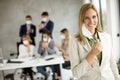 Attractive vusiness woman taking off her protective facial mask and looking at the camera with her team members sitting in Royalty Free Stock Photo