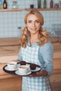 attractive waitress in apron holding tray with cups of coffee and smiling