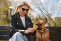 Beautiful young blonde woman sitting on a bench and feeding a dog with ice cream. Cute little bulldog puppy enjoying the dessert Royalty Free Stock Photo