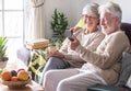 Attractive white-haired senior couple relaxing at home on the sofa looking together at smartphone in video call with family or Royalty Free Stock Photo