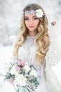 Attractive winter girl in a white outfit in a snow forest with beautiful flowers on her head and a bouquet Royalty Free Stock Photo