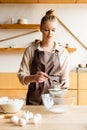 Attractive woman in apron sieving flour