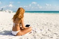 Girl in bikini sitting at the beach using a tablet computer