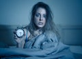 Attractive woman in bed showing alarm clock to camera feeling worried, stressed and sleepless