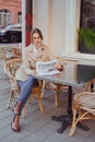 Attractive woman in beige coat reading newspaper in outdoors cafe Royalty Free Stock Photo