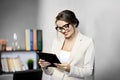 Attractive woman in black-framed glasses is smiling while reading or watching something on digital tablet Royalty Free Stock Photo
