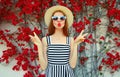 Attractive woman blowing red lips sending sweet air kiss wearing a summer straw hat over red flowers Royalty Free Stock Photo