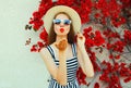 Attractive woman blowing red lips sending sweet air kiss wearing a summer straw hat over red flowers Royalty Free Stock Photo