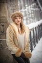 Attractive woman with brown fur cap and jacket enjoying the winter. Side view of fashionable blonde girl posing against bridge Royalty Free Stock Photo