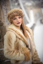 Attractive woman with brown fur cap and jacket enjoying the winter. Side view of fashionable blonde girl posing against bridge Royalty Free Stock Photo