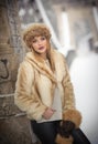 Attractive woman with brown fur cap and jacket enjoying the winter. Side view of fashionable blonde girl posing against bridge Royalty Free Stock Photo